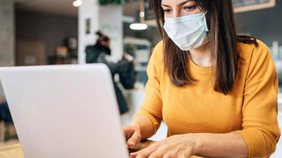 woman with mask on working on laptop